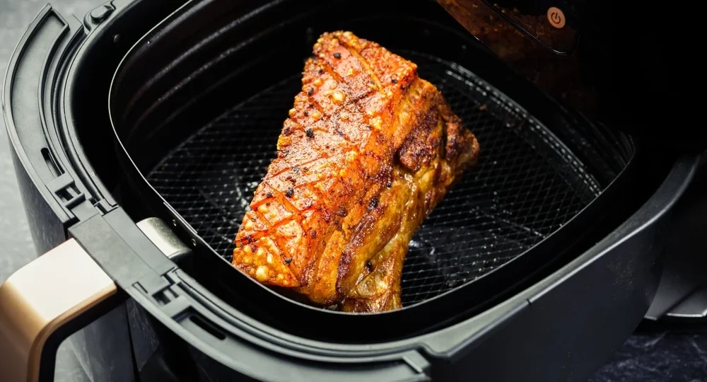 Uma suculenta peça de Panceta Suína Frimesa recém-assada dentro do cesto de uma air fryer. A carne apresenta um tom dourado apetitoso, com a pele superior cortada em formato quadriculado e com textura visivelmente crocante e pururucada.
