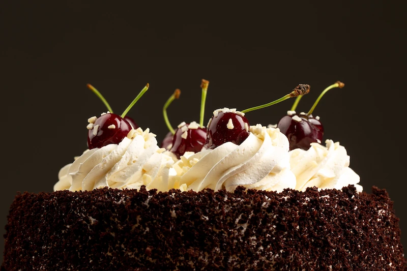 Close do topo de um bolo de chocolate decorado com cobertura de chantilly e cerejas frescas.